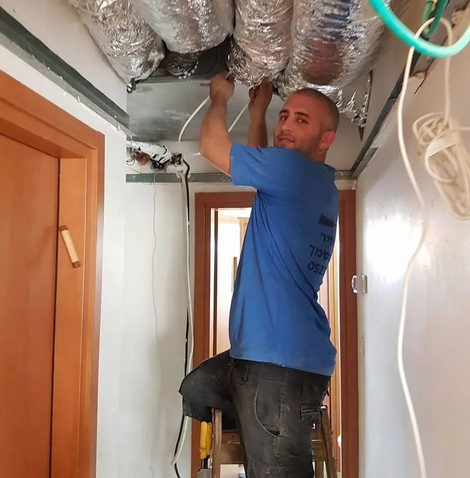 טכנאי עובד על חיבור תעלות מיזוג מעל תקרת גבס